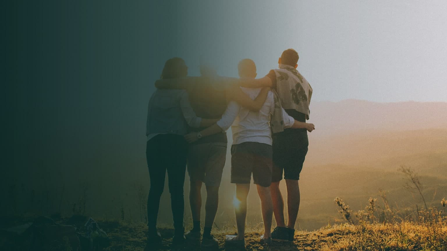 Four friends embracing in a natural landscape at sunset